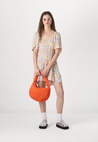 Blommig minikjol med puffärmar i pastellfärger, ihopparad med en texturerad orange väska och metalliska slip-on-skor. Vita glasögon fulländar looken.