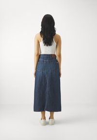Lunga gonna di jeans con lavaggio scuro, vita alta e due tasche posteriori; abbinata a sneakers bianche e a un top fitted bianco.
