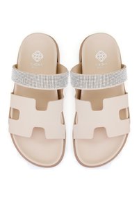 Sandales à glissière beiges avec une semelle en caoutchouc, présentant deux découpes et une lanière métallique ornée de strass. Logo de la marque visible.