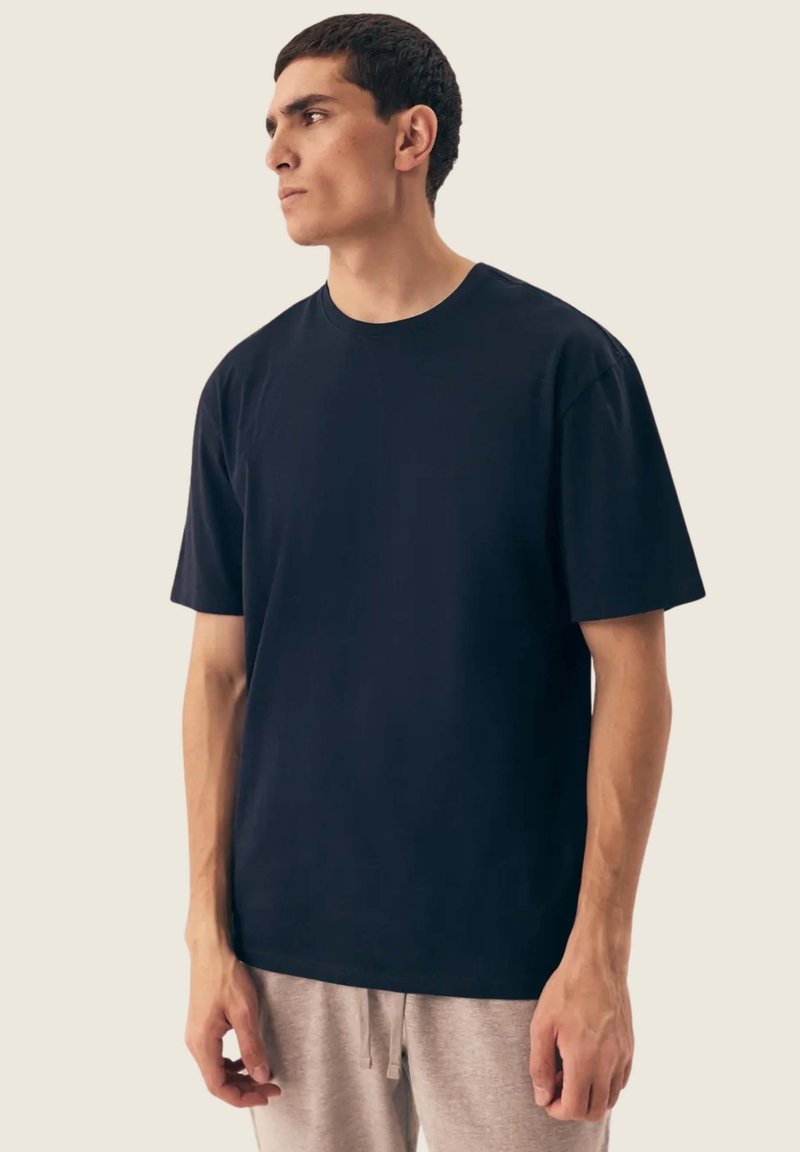 Granatowy t-shirt z krótkim rękawem wykonany z bawełny, z okrągłym dekoltem, luźnym krojem, gładką teksturą i prostym wzornictwem. Noszony z szarymi dresami.