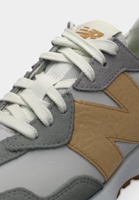 Close-up van een grijze en beige sneaker met witte veters en een getextureerd "N"-logo aan de zijkant.