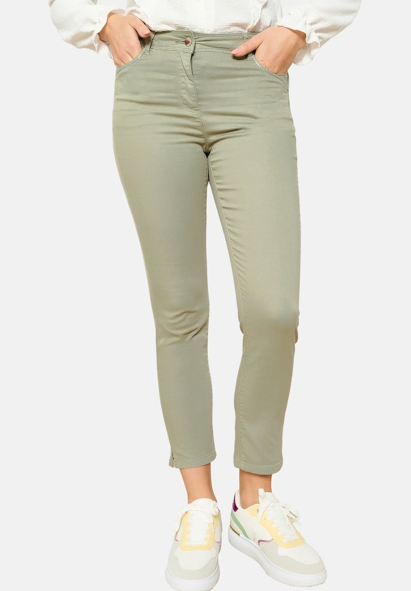 Zelene slim-fit hlače z gladko teksturo, petimi žepi in gumbom za zapiranje. Kombinirane z belimi in pastelno obarvanimi športnimi copati.