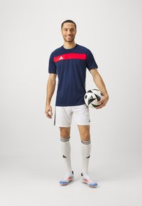 Adidas navy soccer jersey with red stripe, white shorts, and striped socks. Player holds a black and white soccer ball.