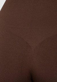Bruine geribbelde leggings met een gladde textuur en een hoge tailleband, die een strakke pasvorm en minimale details bieden.