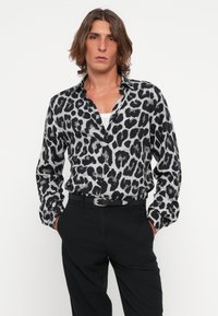 Svart og grå leopardmønstret skjorte med kragehals, lange ermer og løs passform, paret med svarte bukser og et belte.