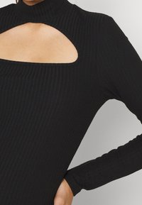 Maglia nera a maniche lunghe con colletto alto e un'apertura rettangolare sul petto. Texture liscia, forma aderente, cuciture dettagliate.