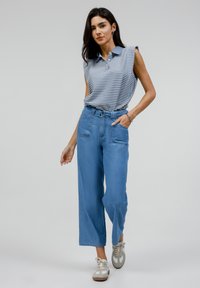 Polo majica brez rokavov z modro-belimi črtami, v kombinaciji z visokim pasom svetlih denim hlačami. Ima široke noge in stranske žepe.