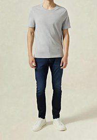 Camiseta gris de manga corta combinada con vaqueros azul oscuro y zapatillas blancas sin cordones, con un ajuste clásico y líneas limpias.