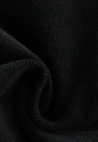 Tissu en velours côtelé noir avec une texture côtelée fine et verticale, surface lisse et subtil éclat, disposé dans une forme douce et fluide.