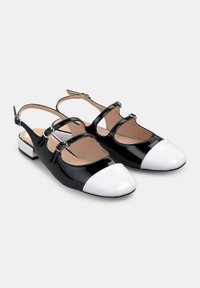 Schwarze Lackleder-Slingback-Schuhe mit weißen Spitzenschuhen, die drei dekorative Schnallen und einen niedrigen Blockabsatz aufweisen.