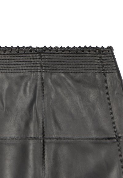 Gros plan sur une jupe en cuir noir avec des coutures horizontales près du haut et un détail de bordure nouée le long de la ceinture.