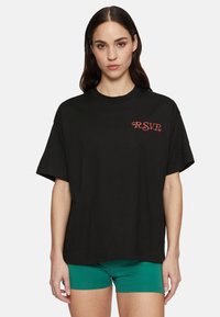 Camiseta de algodón negra con mangas cortas, presenta un logo bordado en rojo "R.S.V.P." en el frente. Cuello redondo, corte relajado.