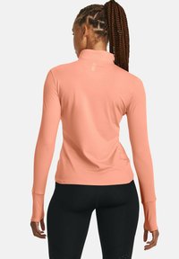 Langärmliges, hochgeschlossenes, tailliertes Oberteil aus leichtem pinkfarbenem Stoff mit glatter Textur, das Daumenlöcher und ein dezentes Logo auf der Rückseite aufweist.