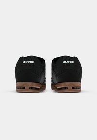 Sorte skate sko med polstret krave, gummisål og brune accenter. Har logo på hælen og ventilationshuller på siderne.