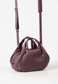 Piccola borsa a tracolla in pelle viola con design piegato e tracolla regolabile, in piedi su uno sfondo bianco.