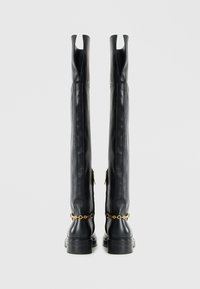 Black leather thigh-high boots with a sleek design, side zippers, and a gold chain accent at the ankle. Square toe and chunky heel.