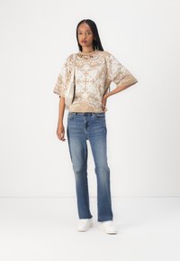 Beige mønstrete topp med hvite blomstermotiver, vide ermer, sammen med blå vide jeans og hvite sneakers. Minimalistisk kremfarget veske.