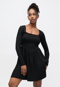 Czarna prążkowana sukienka z długim rękawem, kwadratowym dekoltem, dopasowanym gorsetem i rozkloszowanym dołem. Materiał ma gładką fakturę, zapewniając luźne dopasowanie.