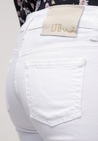 Jeans de mezclilla blanca con un diseño ajustado, que presentan una etiqueta de cuero LTB en la parte trasera y dos bolsillos traseros con sutiles detalles de costura.