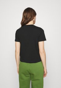 Černé bavlněné tričko s kulatým výstřihem a krátkými rukávy, stylizované se zelenými tepláky, zobrazené zezadu, ukazující uvolněný střih.