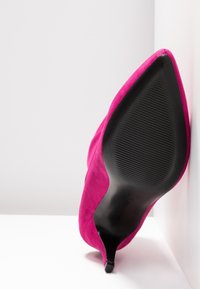 Chaussure à talon haut rose vif vue de la semelle, avec une semelle en caoutchouc noire pointue et un talon court et fin.