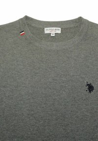 Grå stickad tröja med rundad halsringning. Har en liten mörk logotyp på vänster sida och en trikromatisk etikett nära kragen. Storlek medium.