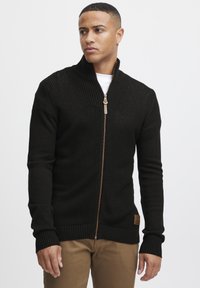 Schwarzer Zip-Up-Pullover aus strukturiertem Strickstoff, mit gerippten Bündchen und Saum, hoher Kragen und einem bronzefarbenen Reißverschluss.