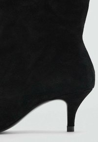 Bottine en daim noir avec un talon stiletto fin, une forme effilée et une texture lisse. Design minimaliste sans décorations visibles.