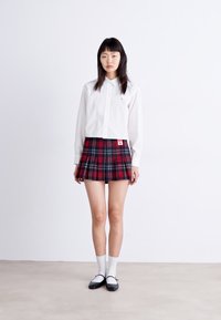 White button-up shirt, tartan pleated red and black skirt, white ankle socks, and black shoes with white accents. Smooth fabric, casual design.