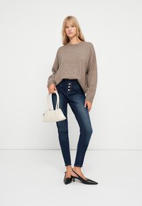 Brun strikkegenser, høyt liv blå jeans med knappdetaljer, svarte slingback sko og en liten hvit veske. Enkel, uformell antrekk.