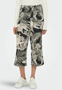 Black and white cropped pants with a floral and leaf pattern, featuring an elastic waistband and side pockets, paired with white sneakers.