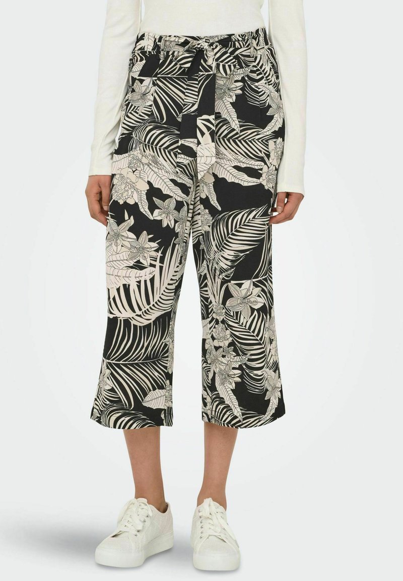Black and white cropped pants with a floral and leaf pattern, featuring an elastic waistband and side pockets, paired with white sneakers.