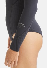 Combinaison de plongée marine avec des panneaux texturés et une finition lisse. Comprend des manches longues et un détail imprimé "SURF CAPSULE". Coupe ajustée pour le confort.
