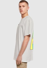 Lys grå bomulds t-shirt med et farverigt grafikdesign på ryggen. Løs pasform med korte ærmer og rund halsudskæring.