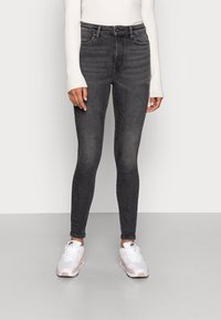 Jeans negros slim-fit con cintura alta, que presentan un sutil desvanecimiento y un cierre de botón clásico, combinados con zapatillas blancas.