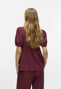 Blusa burgundy con maniche a sbuffo, tessuto testurizzato e vita arricciata, abbinata a pantaloni coordinati, vista dalla schiena.