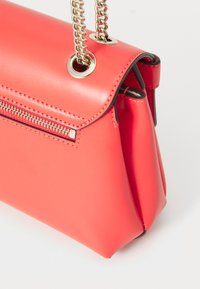 Coral pink handbag made of smooth synthetic material, featuring a chain strap, zip pocket, and a structured design with a metallic accent.