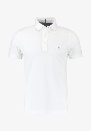 Polo blanc avec une patte de boutonnage à trois boutons, manches courtes, et un petit logo coloré sur la poitrine gauche. Confectionné en tissu respirant.