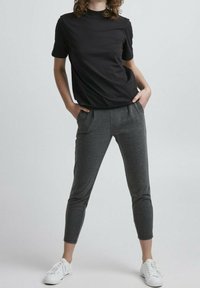 T-shirt noir à manches courtes associé à un pantalon gris fuselé avec poches, stylisé avec des sneakers blanches. Tenue simple et décontractée.