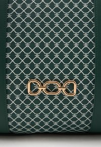 Πράσινη τσάντα με λευκό γεωμετρικό μοτίβο, διαθέτει χρυσή αλυσίδα. Υφασμάτινη τσάντα με υφή και δομημένο στυλ.