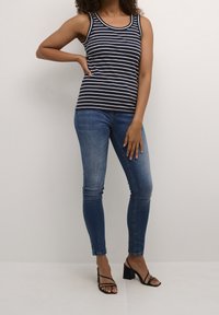 Mörkblå och vitrandig linne med ribbad textur, kombinerat med åtsittande blå denimjeans och svarta sandaler med remmar.