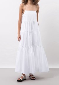 Bílá bavlněná maxi šaty s nastavovacími ramínky, vrstveným designem a nařaseným pasem. V kombinaci s plochými černými sandály.