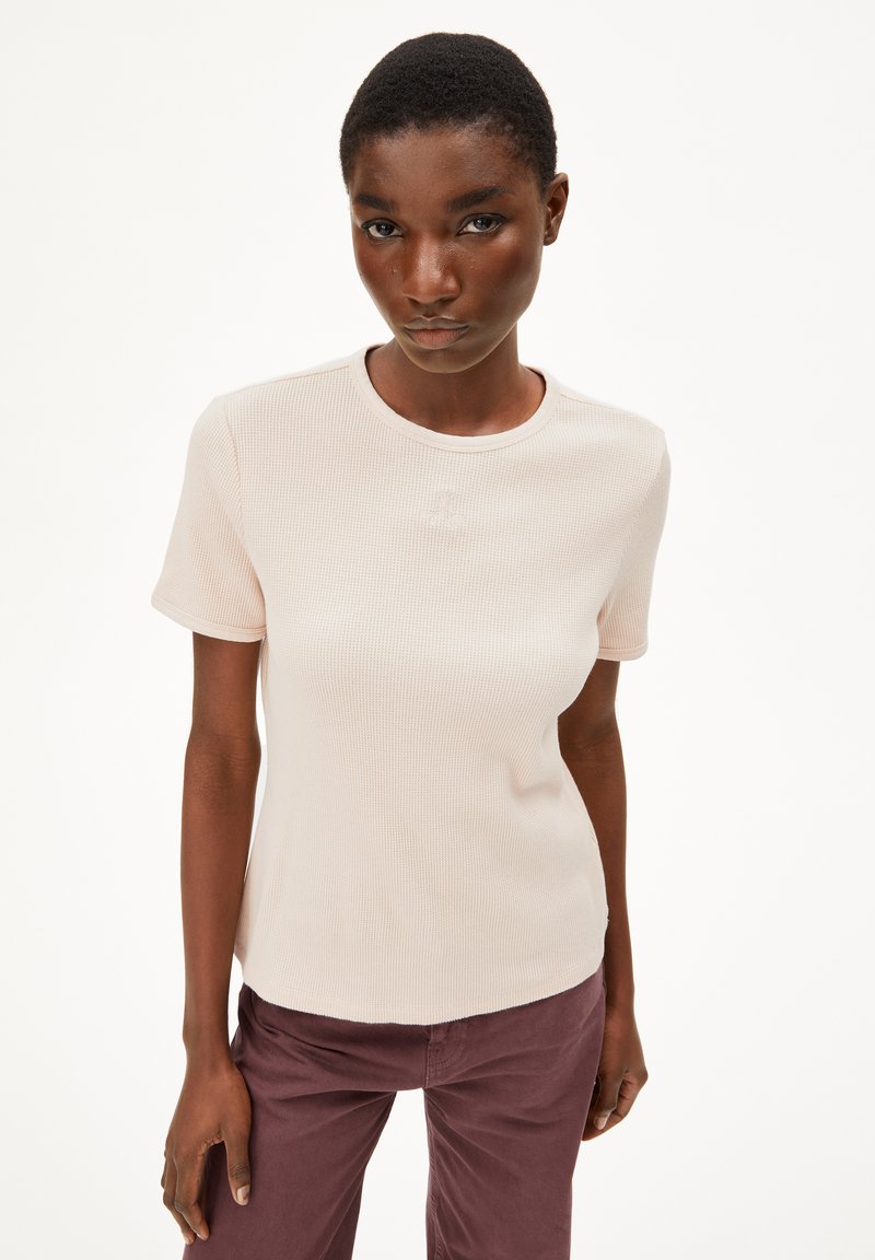 Lichtbeige geribde T-shirt met korte mouwen en een ronde halslijn, gecombineerd met mauve broek. De stof heeft een gestructureerd patroon.