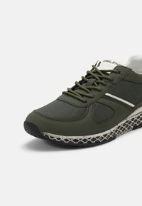 Green athletic shoe with a textured surface, featuring a reinforced toe, laces, and a lightweight sole with a patterned grip.
