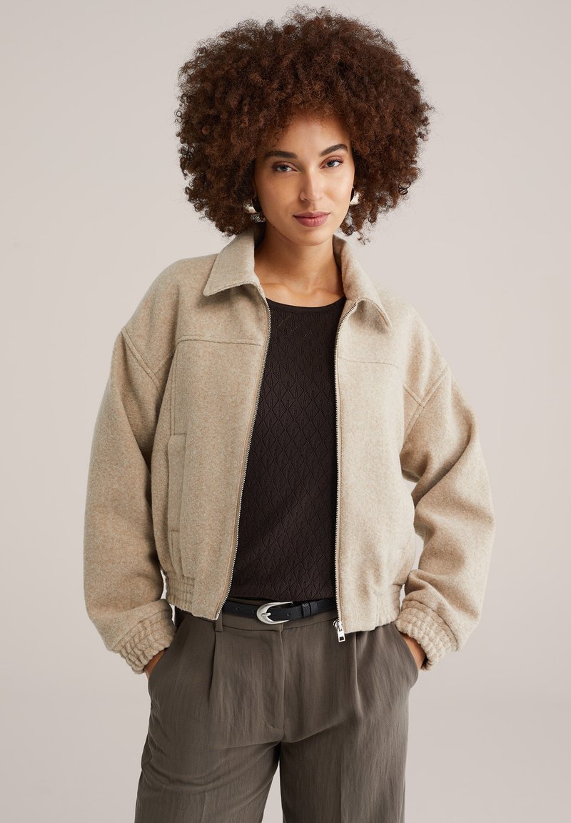 Béžová bomber bunda na zip s límcem, žebrovanými manžetami a texturovanou látkou. Nositelná přes tmavý dlouhý rukáv a kalhoty.