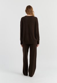 Maglione marrone oversize con scollatura rotonda e maniche ampie, abbinato a pantaloni a gamba larga coordinati, realizzati in morbido tessuto a maglia.