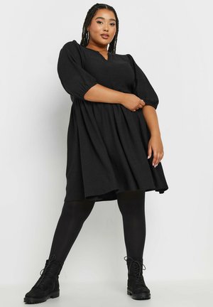 Black puff-sleeve dress with a V-neck, featuring a gathered skirt and textured fabric, paired with black lace-up ankle boots.