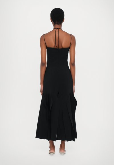 Μαύρο, αμάνικο φόρεμα με εφαρμοστό κορσέ και φούστα σε άλματα, η οποία διαθέτει κάθετες πτυχώσεις. Λεπτές τιράντες και χαμηλή πλάτη.