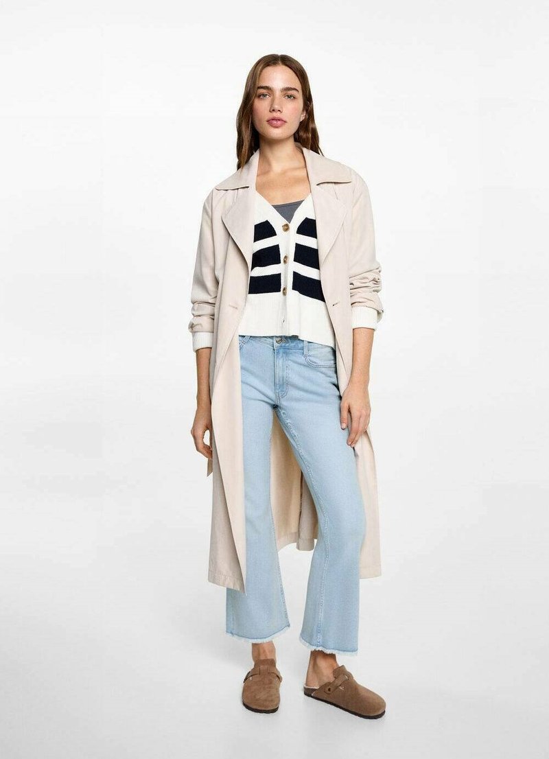 Trench beige sobre un cárdigan a rayas blancas y marinas, jeans cortos de mezclilla azul claro y zapatos marrones de slip-on. Diseño sencillo y texturas suaves.