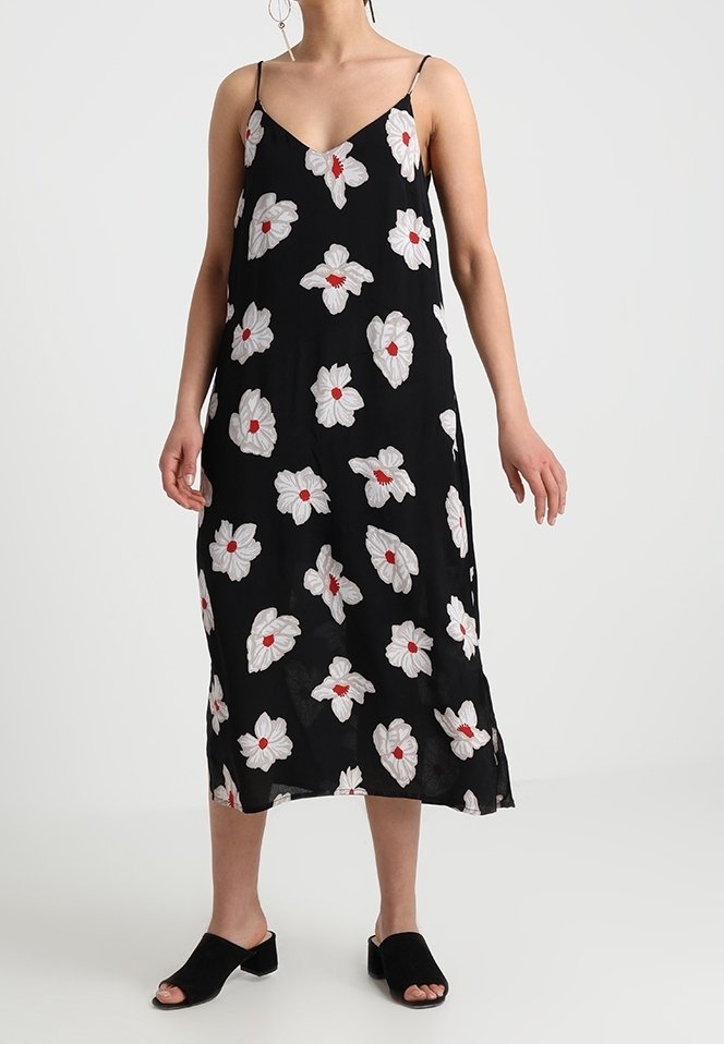 Robe sans manches noire avec des motifs floraux blancs et des centres rouges, en tissu léger, dotée d'une coupe décontractée et d'un ourlet à la cheville.